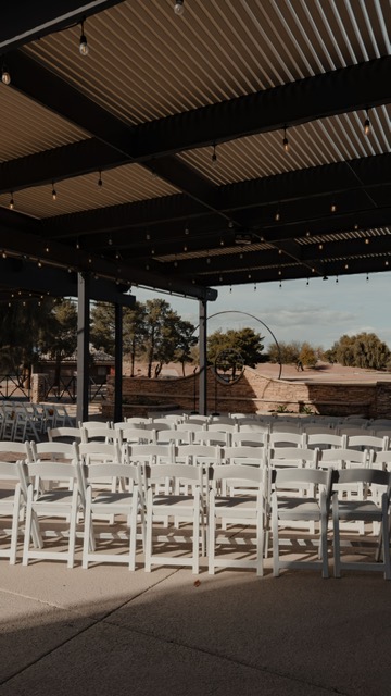 White folding chairs arranged for a ceremony on a covered patio with string lights