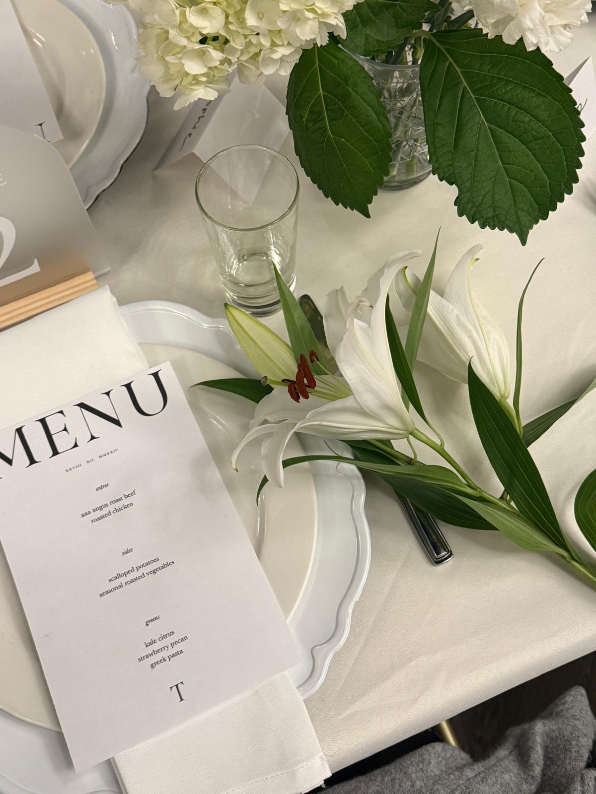 Place setting with scalloped charger plate, printed menu card, cloth napkin and white lily